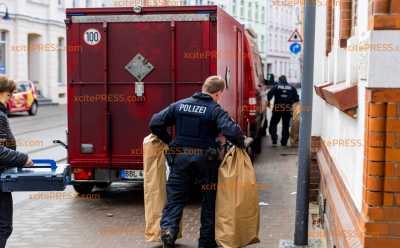 Polizei durchsucht mehrere Wohnungen und Fahrzeuge und beschlagnahmt Pyrotechnik: Ermittler tragen mehrere Papiertüten mit sichergestelltem Inhalt zu gepanzertem Fahrzeug der Sprengstoffspezialisten